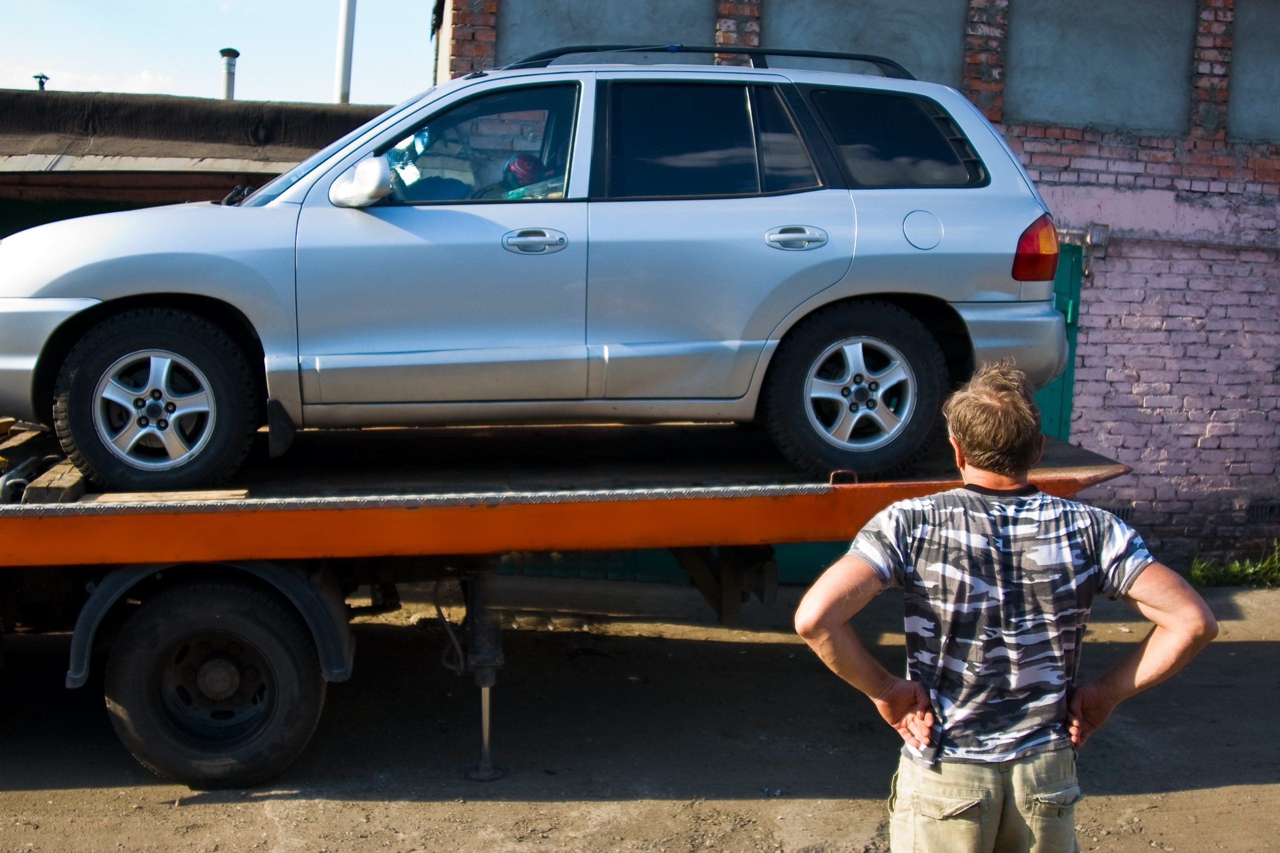 A man stands in front of his SUV being towed.