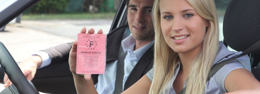 A blonde teenage girl with her learner's permit, sitting in the front seat of a car.
