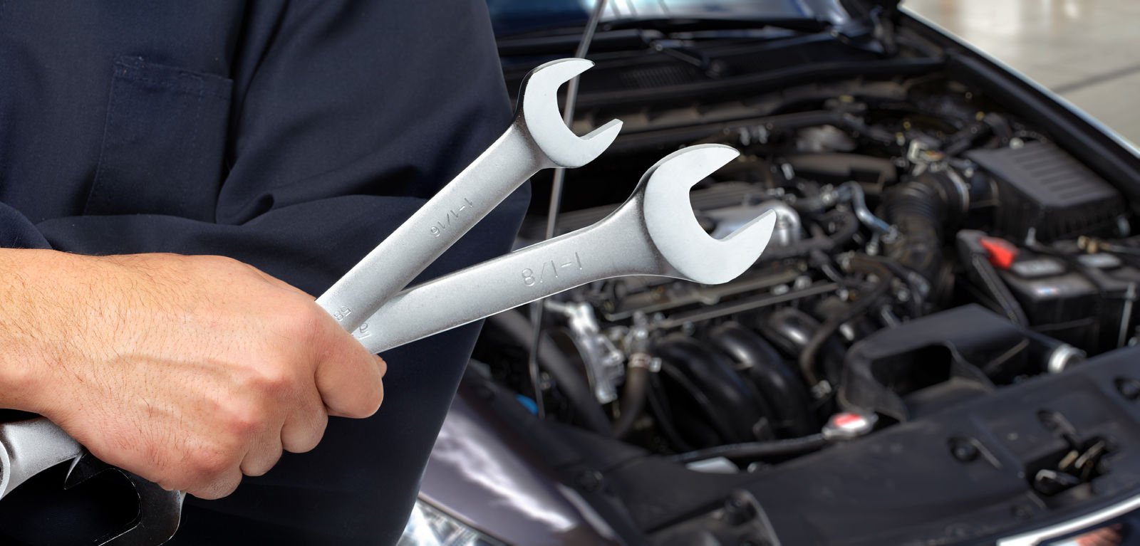 Mechanic standing in front of car with two wrenches in hand. Car repair.