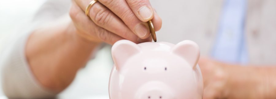 savings, money, annuity insurance, retirement and people concept - close up of senior woman hand putting coin into piggy bank