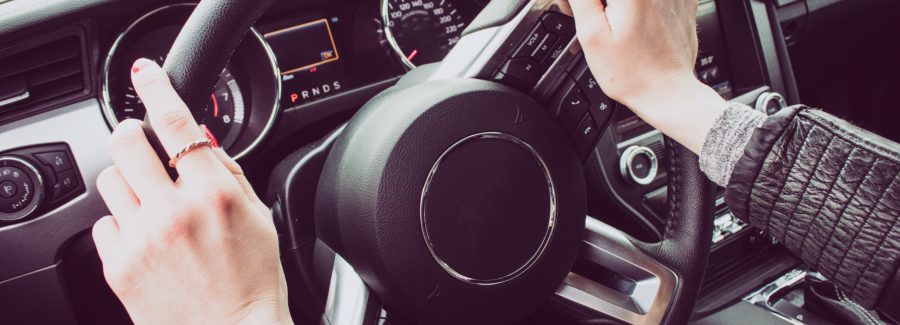 Close up image of female driver hands on the steering wheel. Red painted nails.