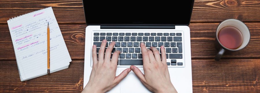 A laptop next to a notebook and cup of tea